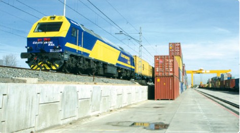 Locomotora de Continental Rail junto a contenedores apilados y grúa pórtico en terminal.